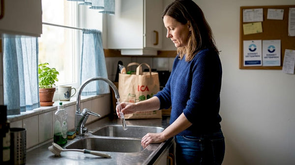 En kvinna tar ett vattenprov från kökskranen hemma.